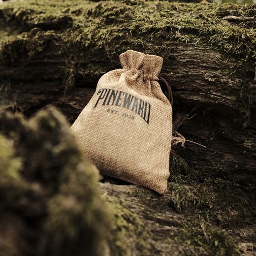 A Pineward burlap pouch on a mossy log, in shadow